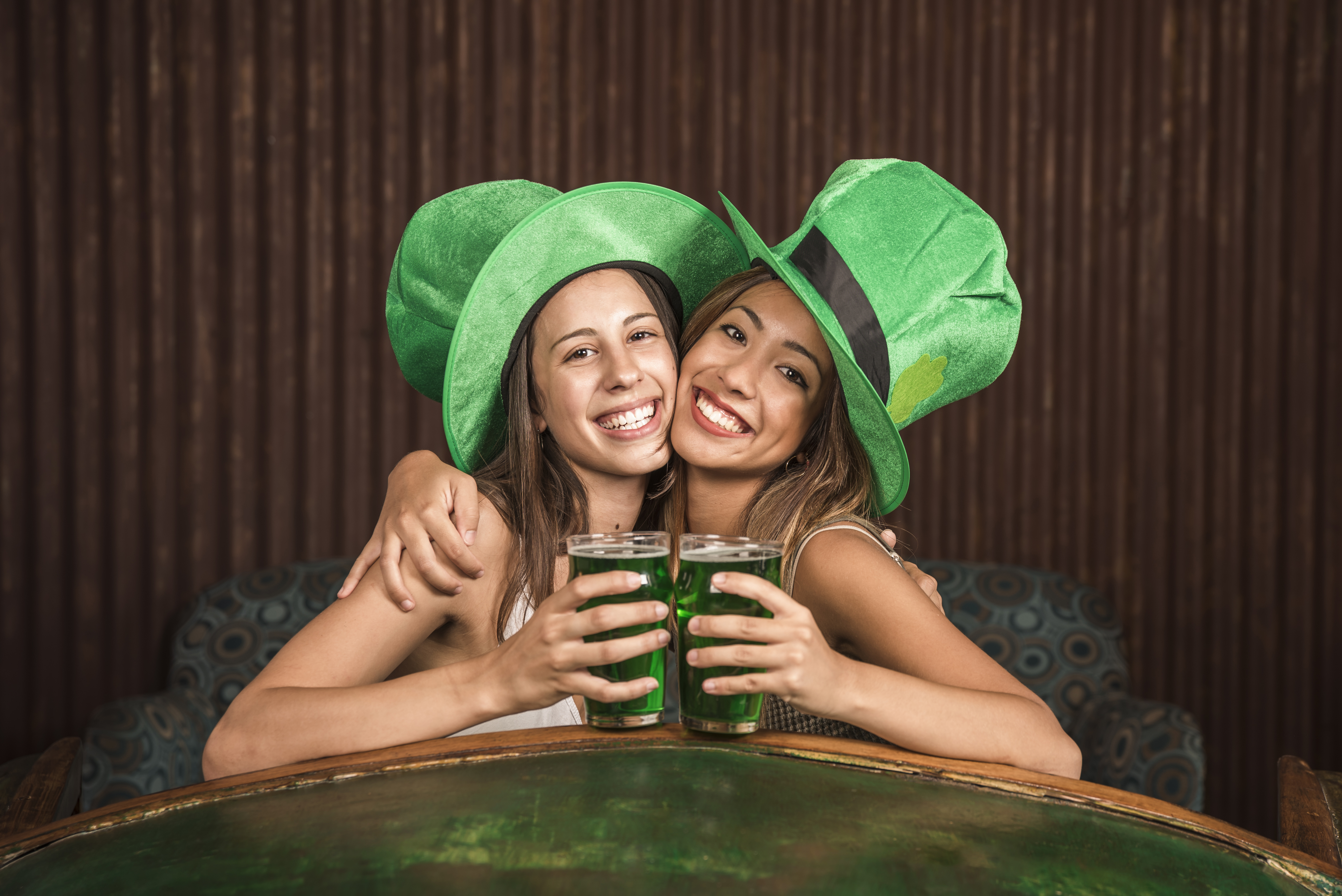cheerful-young-women-hugging-with-glasses-drink-settee-near-table